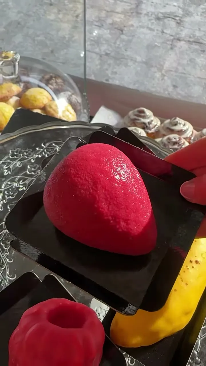 Pastel de mousse rojo con forma de fresa sobre una bandeja negra