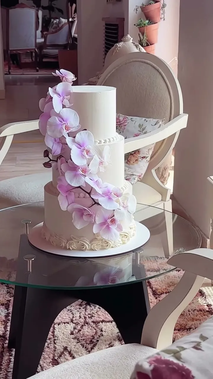 Tarta de boda blanca de tres pisos con una cascada de orquídeas lilas, en un salón