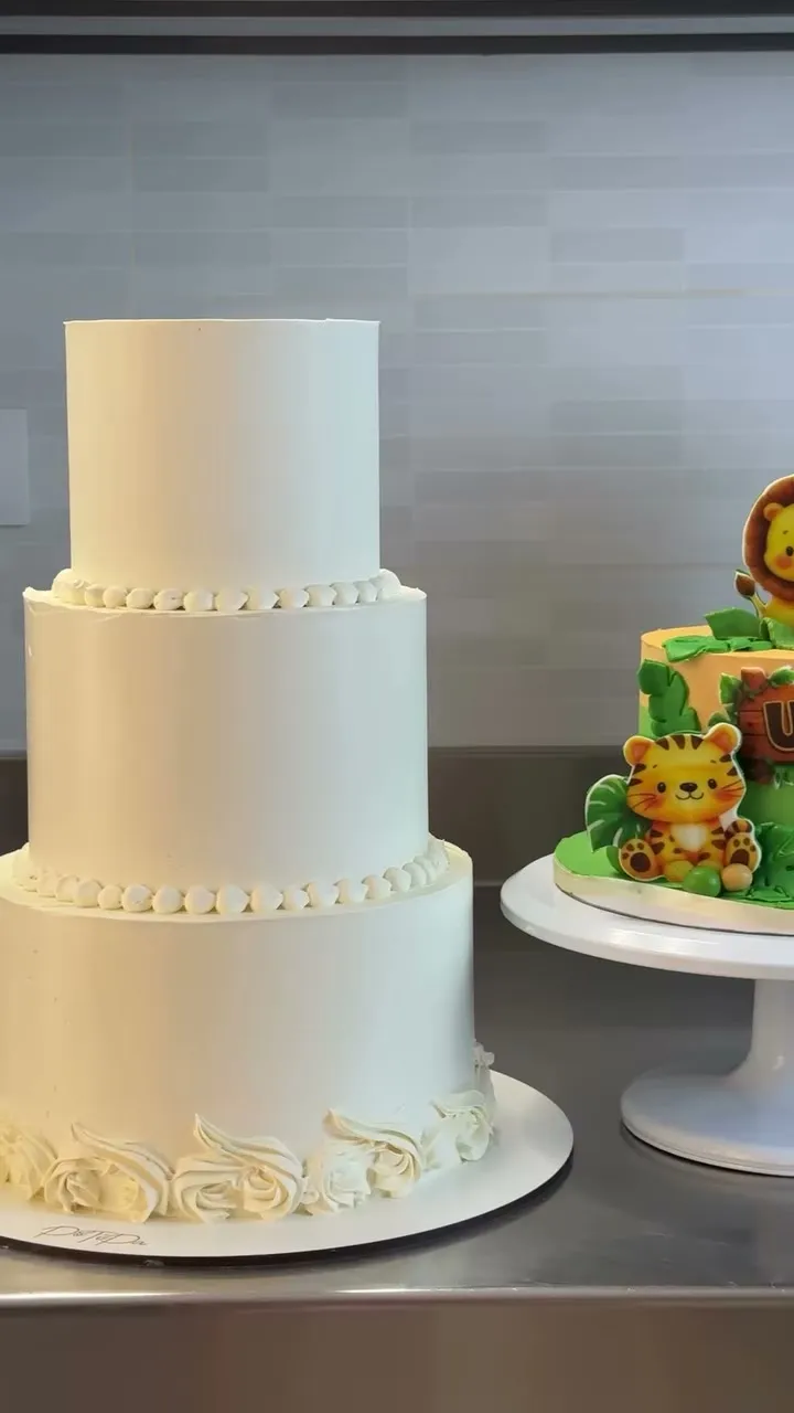 Tarta blanca de tres pisos junto a una tarta infantil con un león de fondant